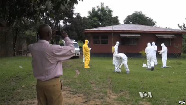 A man takes a photo as a group of people in protective clothing disinfect themselves and each other outside a home.
